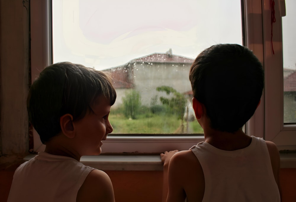 two young boys looking out of a window