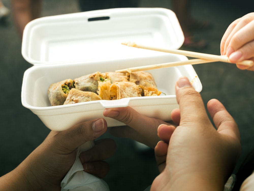 a person holding a container of food with chopsticks in it