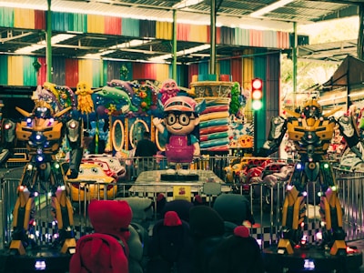 An indoor amusement area featuring colorful decorations with cartoonish designs. There are large robot-like figures positioned prominently alongside vibrant ride-on cars for children. Various colorful designs cover the walls and ceilings, reflecting a playful and fantasy-themed setting.