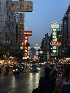 A bustling Bangkok street at dusk filled with colorful signs and lively crowds.