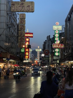 A bustling Bangkok street at dusk filled with colorful signs and lively crowds.