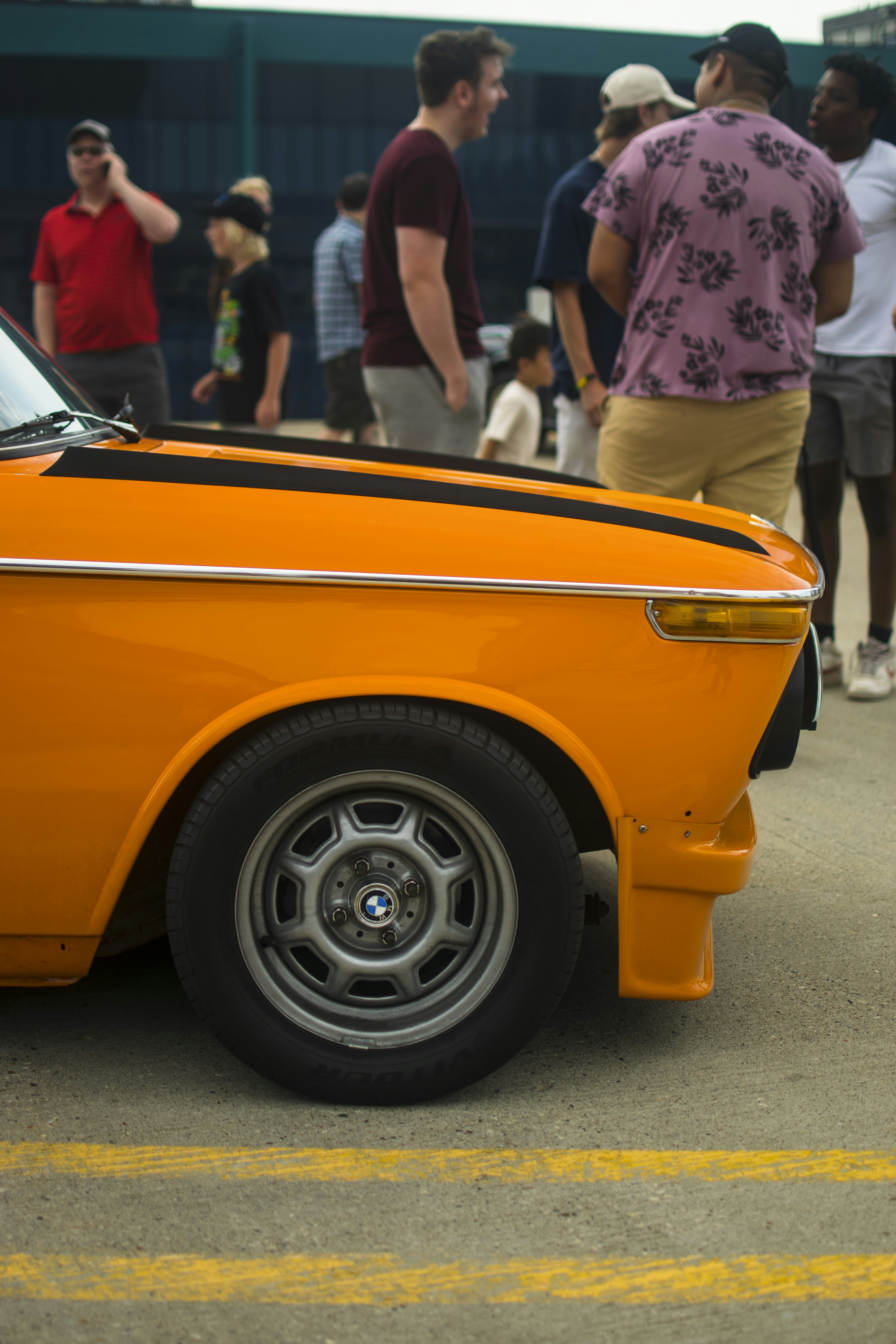a group of people standing around an orange car