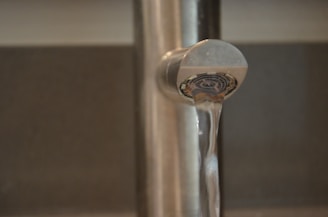A close-up view of a metal faucet with water flowing smoothly from its spout against a blurred background.