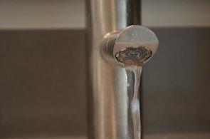A close-up of a wrench tightening a bathroom faucet with water flowing smoothly.