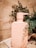 A peach-colored bottle of Monday Conditioner is placed on a stone tile surface, surrounded by green leafy plants. The bottle's design is minimalistic with embossed branding and text indicating it is PETA certified and contains 350ml. The natural background gives a calming and organic feel to the setting.