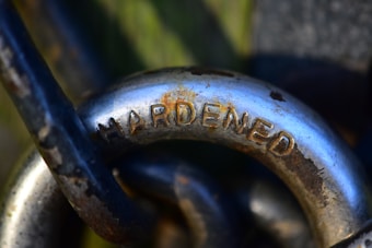 A close-up of a metallic object with the word 'HARDENED' engraved on it, surrounded by other metal components. The surface shows signs of rust and wear, providing a sense of durability and strength.