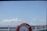 A red life buoy labeled 'AROEIRA' is mounted on the railing of a boat, with a view of a harbor and a city skyline in the background under a clear blue sky.