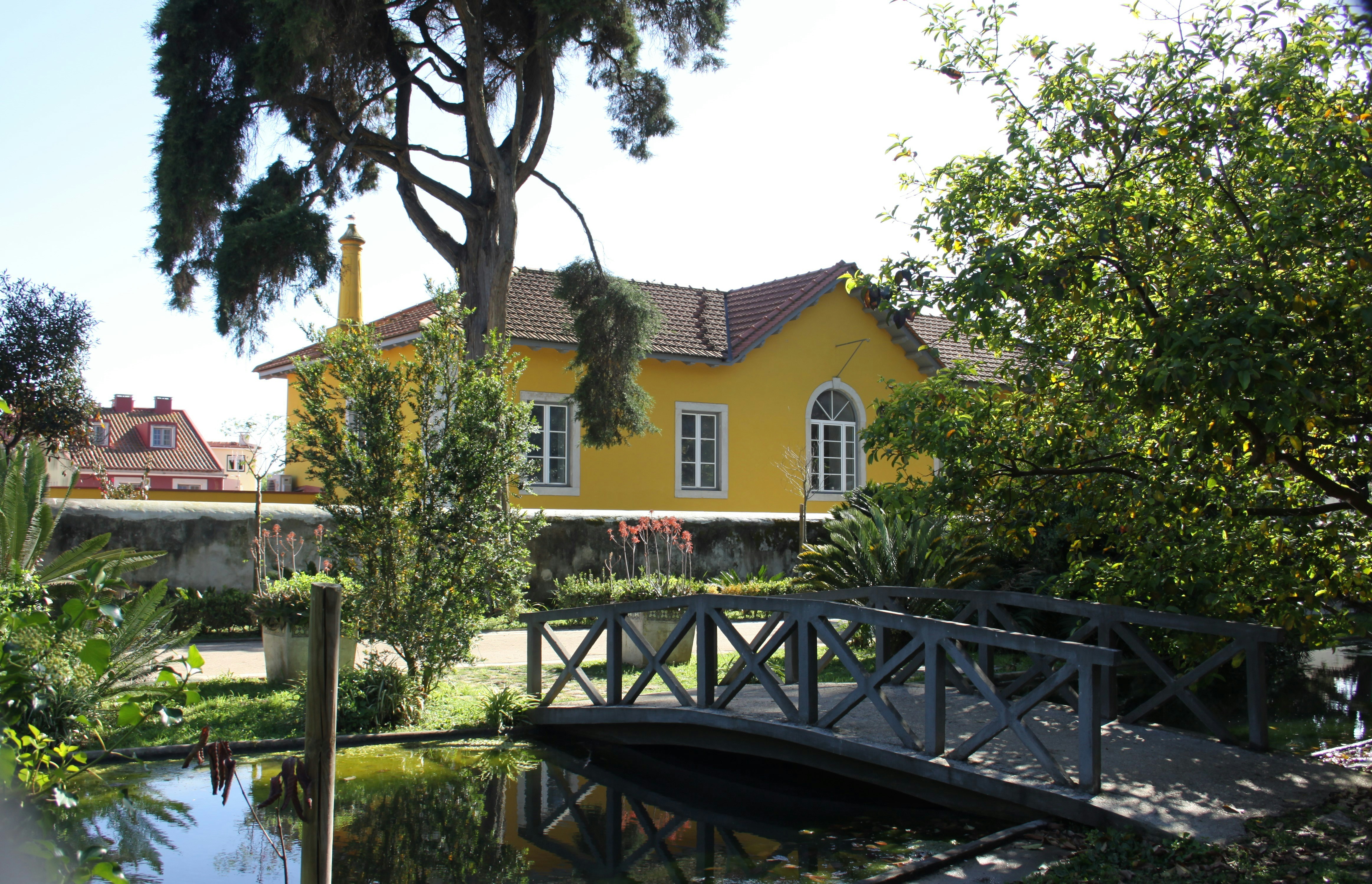 a yellow house with a bridge over a pond, Jardim Botânico Tropical