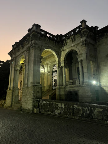 Evening view of the hotel’s stone facade glowing warmly under soft Mediterranean lighting.