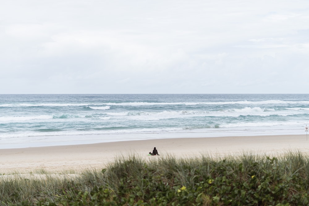 a couple of people sitting on top of a sandy beach