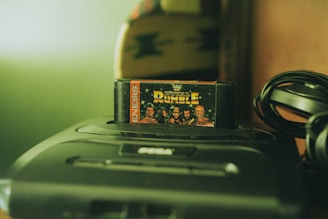 A retro video game console with a cartridge titled 'Royal Rumble' inserted, featuring wrestlers on the cover. The console is a Sega Genesis, and there is a coiled cable next to it. The setting has a nostalgic and vintage feel, with soft lighting.