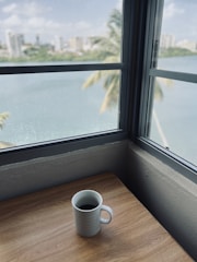 Elegant glass coffee mug resting on a wooden table with city skyline blurred in the background.