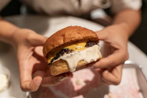 Hand holding a burger with melted cheese stretching out as a bite is taken, capturing the delicious moment.