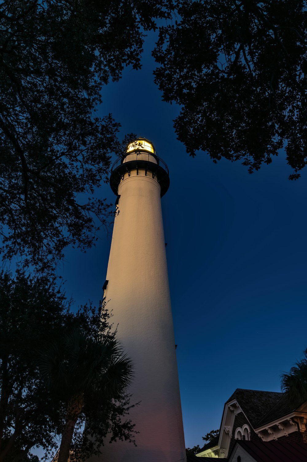 a white light house sitting next to a tree