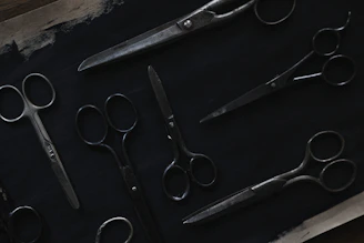 Close-up photo of various scissors laid out on a wooden table, showcasing different styles and sizes.
