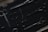A variety of scissors are arranged on a dark surface. The scissors are of different sizes and styles, featuring metal blades and handles. The image is dimly lit, highlighting the metallic sheen against the dark background.