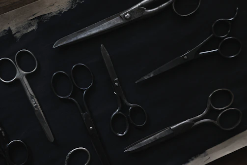 Close-up photo of various scissors laid out on a wooden table, showcasing different styles and sizes.