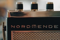 A close-up view of an old-fashioned radio with three black knobs on top and the brand name 'Nordmende' visible. The front features a grid-like speaker pattern.
