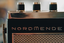 A close-up view of an old-fashioned radio with three black knobs on top and the brand name 'Nordmende' visible. The front features a grid-like speaker pattern.