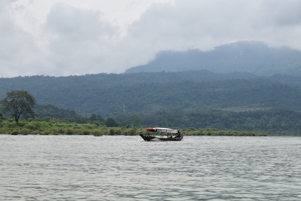 a boat floating on top of a lake next to a lush green hillside