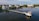 Several upscale waterfront homes are situated along a tranquil waterway, with a long pier extending into the water. There are boats docked at the pier, and the scene reflects a peaceful coastal setting.