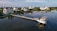 Several upscale waterfront homes are situated along a tranquil waterway, with a long pier extending into the water. There are boats docked at the pier, and the scene reflects a peaceful coastal setting.