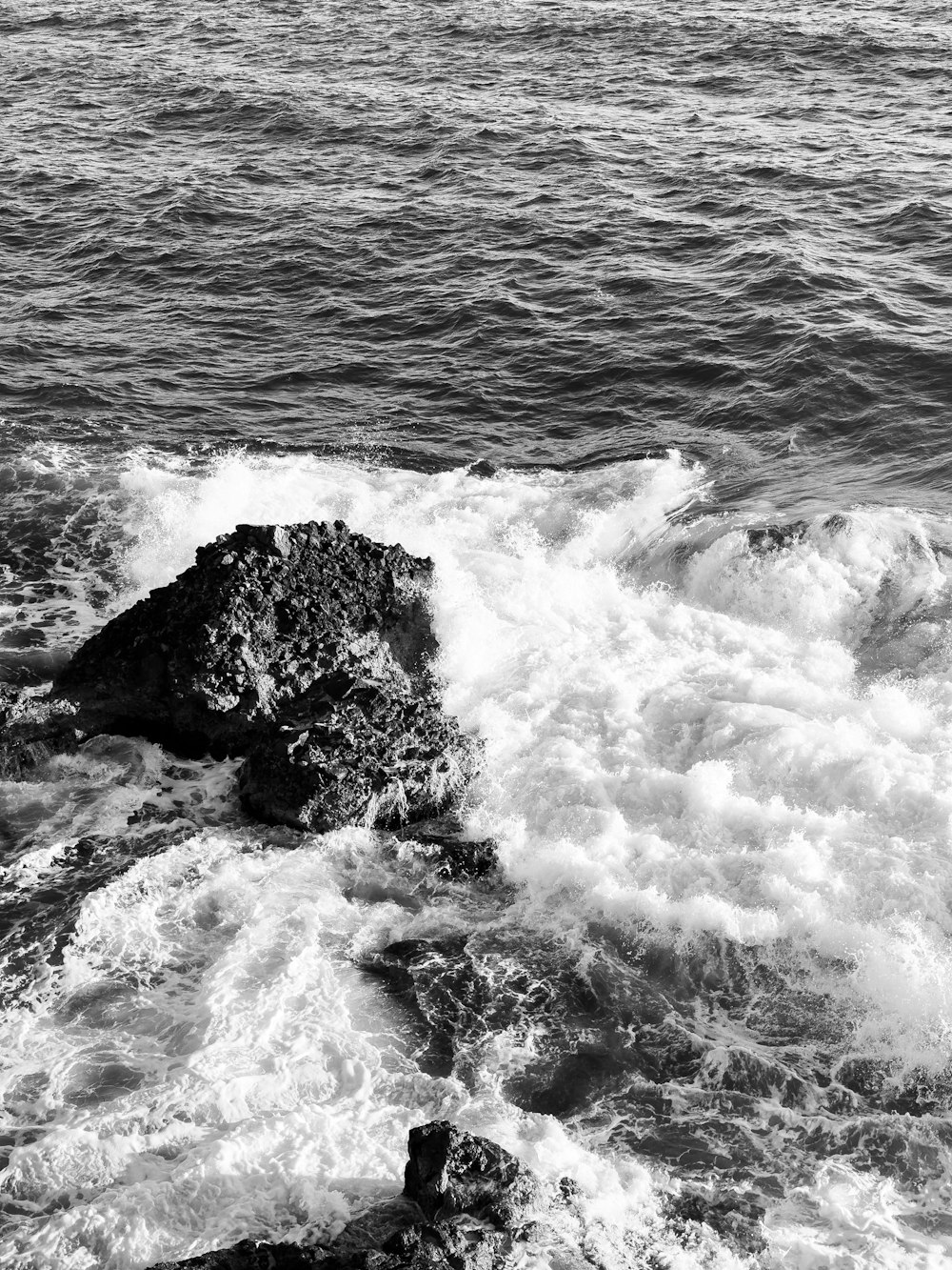 a black and white photo of a rock in the middle of a body of water