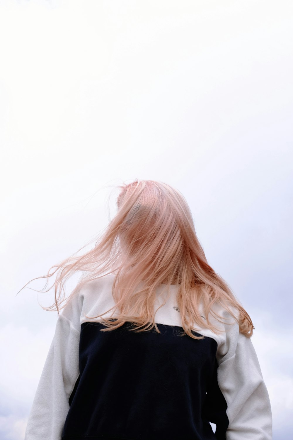 a woman with pink hair standing in front of a cloudy sky