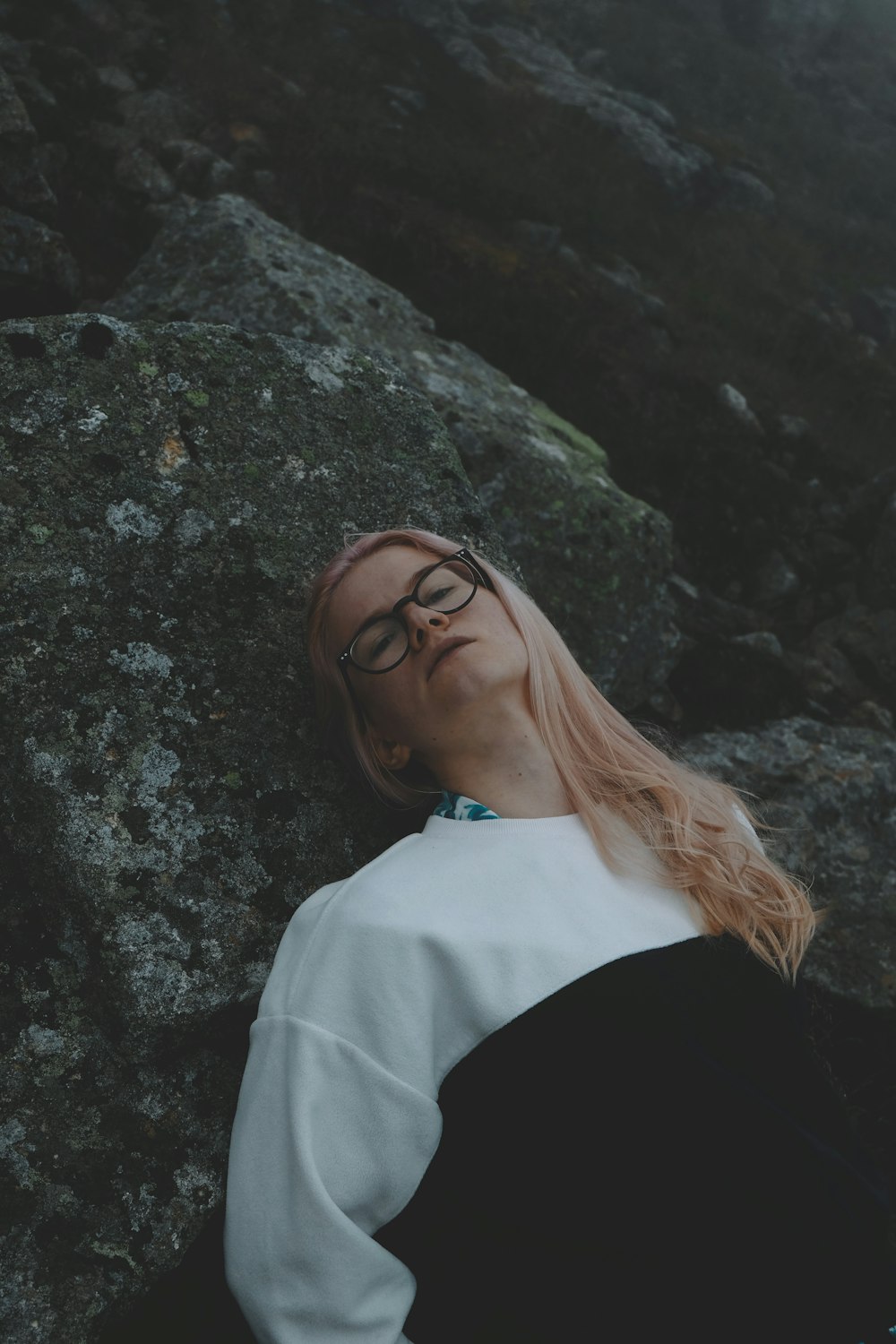 a woman wearing glasses laying on a rock
