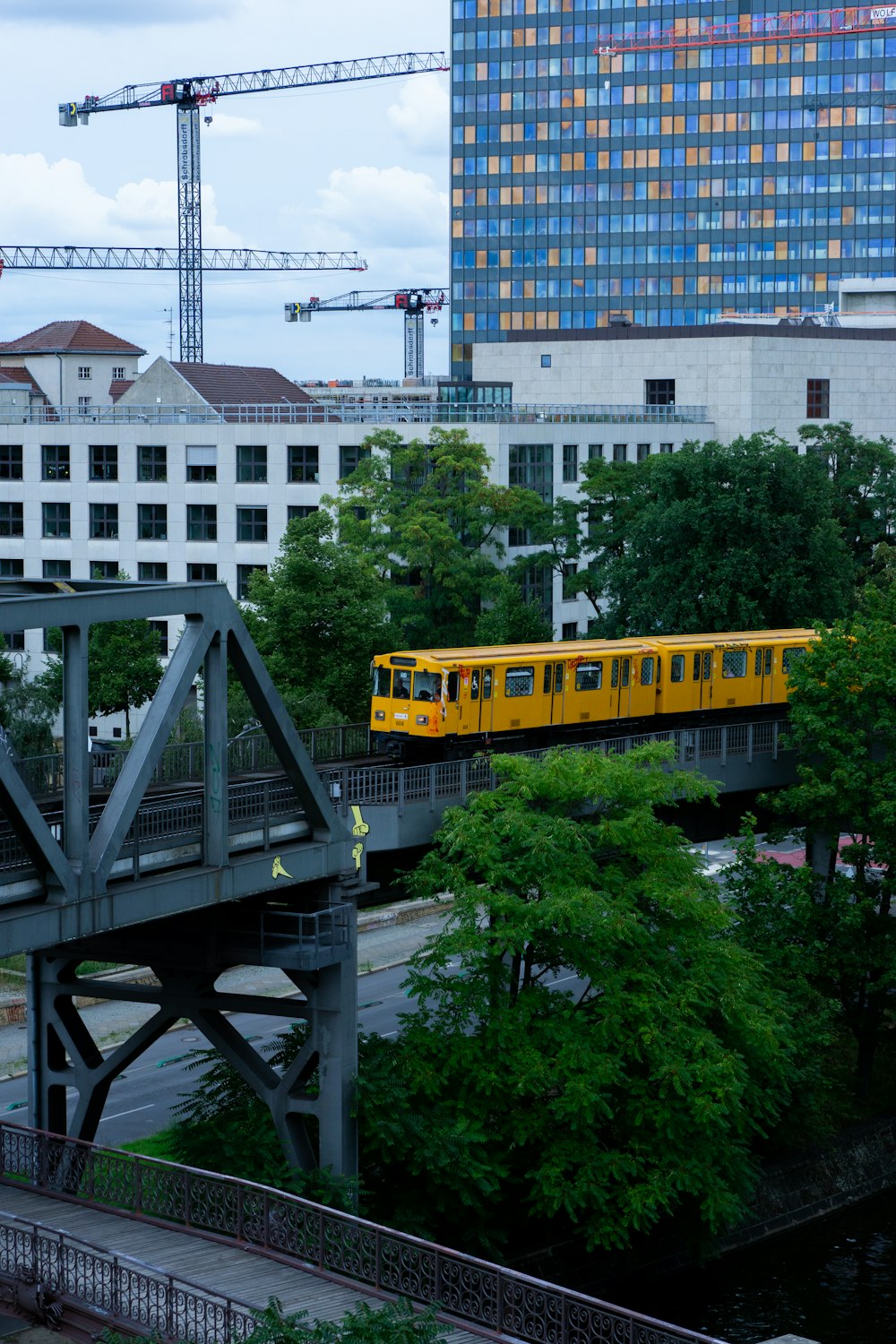 a yellow train traveling over a bridge next to tall buildings
