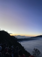Travelers bundled up, smiling as they watch the sun rise from a scenic viewpoint atop Mount Batur.