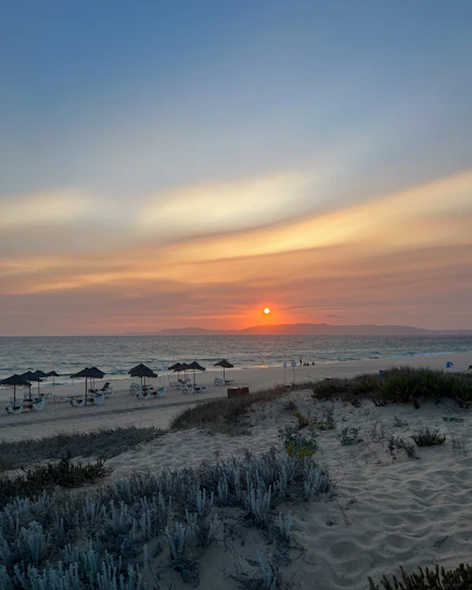 A serene beachfront villa at sunset, with soft sand and gentle waves in the background.