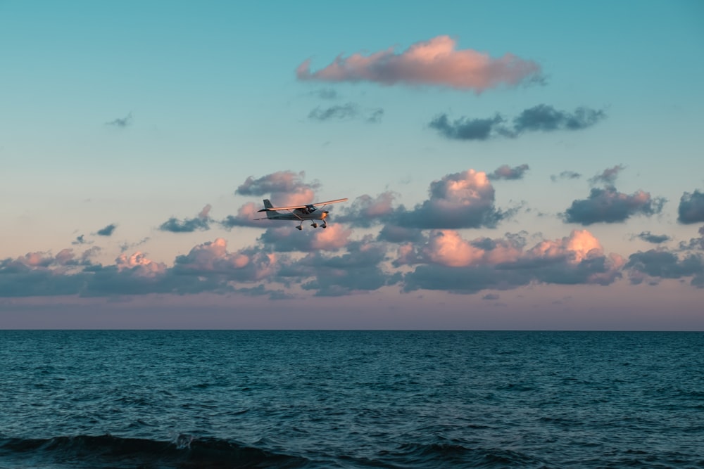 a plane flying over the ocean under a cloudy sky