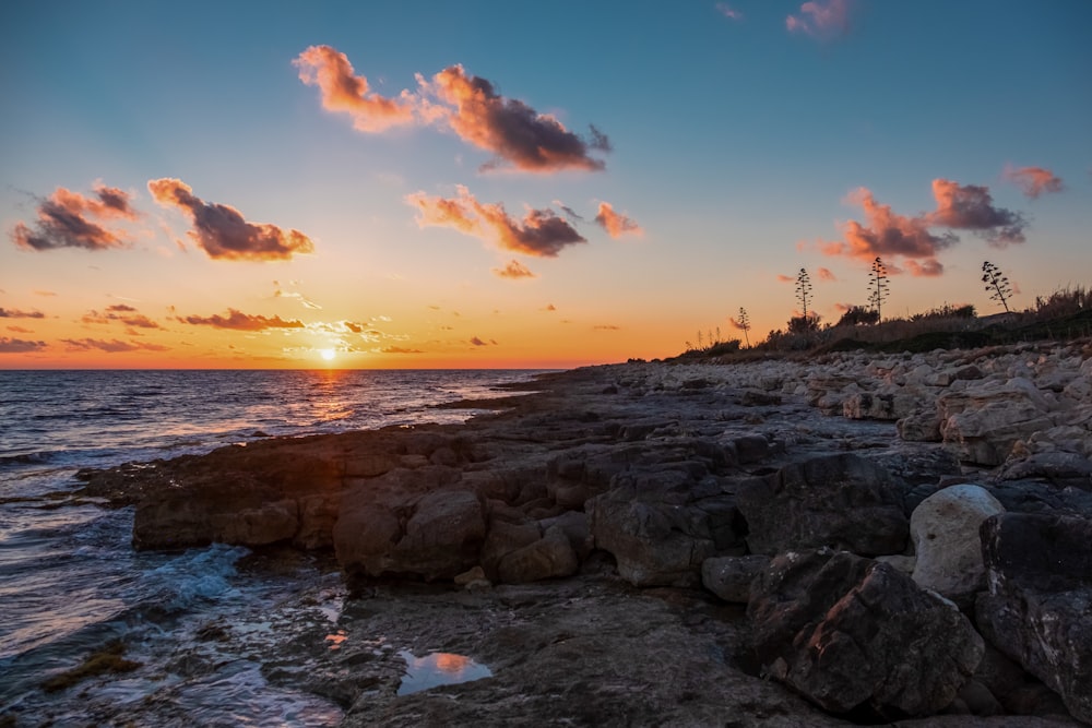 the sun is setting over a rocky shore