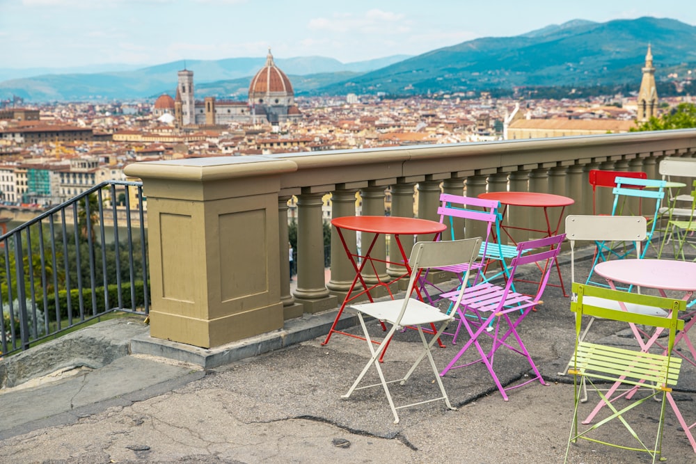 cadeiras e mesas coloridas em uma varanda com vista para uma cidade