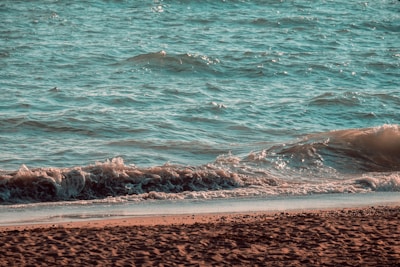 Soft turquoise waves gently rolling onto a sunlit beach at dawn.