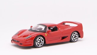 A small red sports car model with sleek aerodynamic design and detailed features, including black and silver wheels and a glossy finish.