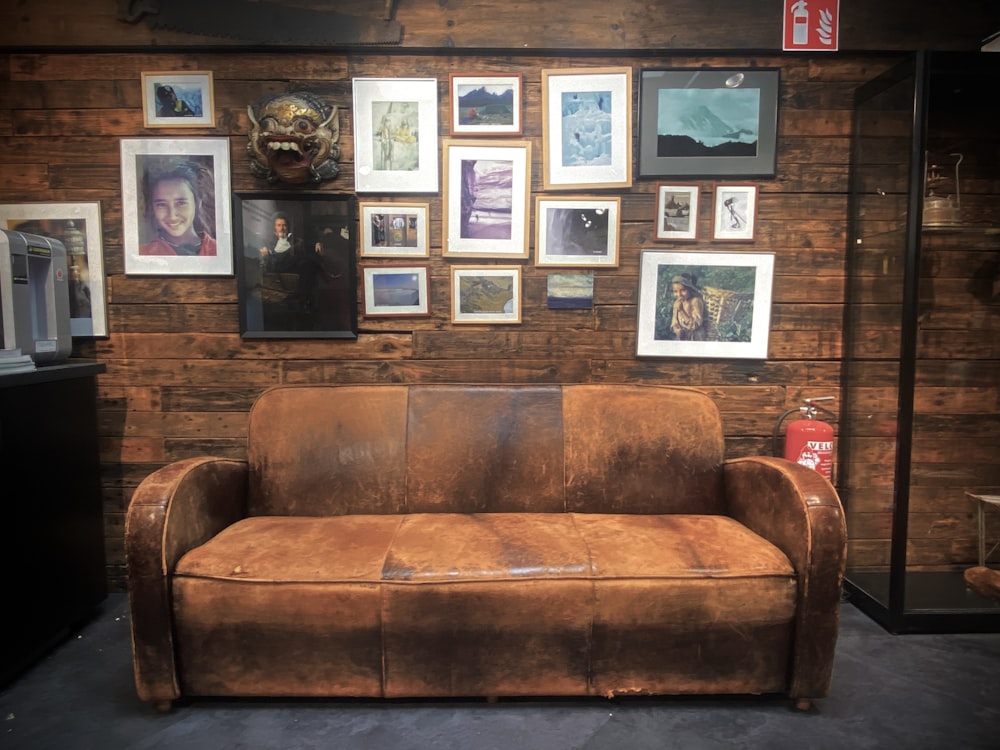 a brown leather couch sitting in front of a wooden wall