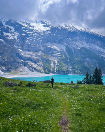 A lone hiker walking a narrow trail along a rocky ridge with wildflowers in bloom.