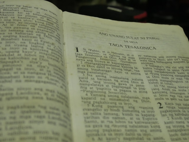 An open book written in Tagalog, specifically a religious text. The visible text mentions 'Ang Unang Sulat Ni Pablo' and 'Taga Tesalonica.' The book is slightly worn, suggesting frequent use.