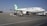 A large commercial airliner branded with the name Mahan Air is parked on an airport tarmac. The aircraft is being serviced with equipment such as a luggage cart nearby. The sky is clear, and the runway is expansive.