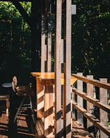 Sunlight filtering through tall trees onto a rustic wooden cabin porch with comfy chairs.