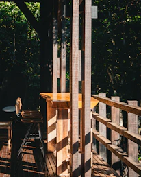 Sunlight filtering through tall pine trees onto a rustic wooden table with fabric swatches and sketches.