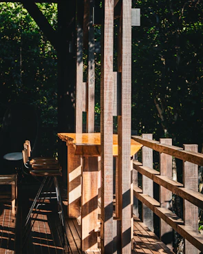 Sunlight filtering through tall trees onto a rustic wooden cabin porch with comfy chairs.