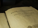 An open book with text in Tagalog, indicating it's a religious script, possibly a Bible. The page shows black printed letters on an aged, yellowish surface.