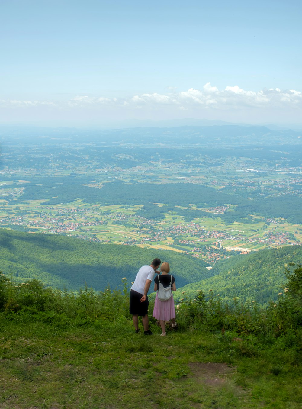 a couple of people standing on top of a lush green hillside