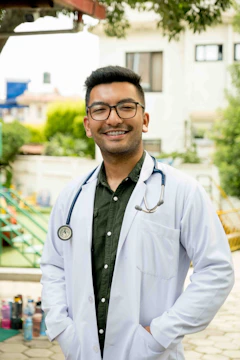 A smiling doctor checking a child's heartbeat under a village tree.