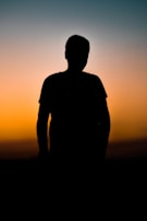 A silhouette of a lone figure standing against a vibrant sunset sky.