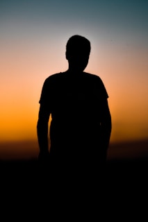 A silhouette of a lone figure standing against a vibrant sunset sky.