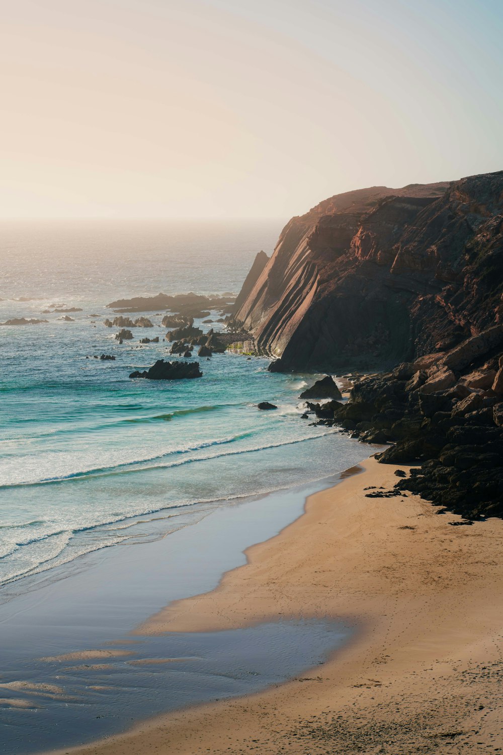 a sandy beach next to a rocky cliff